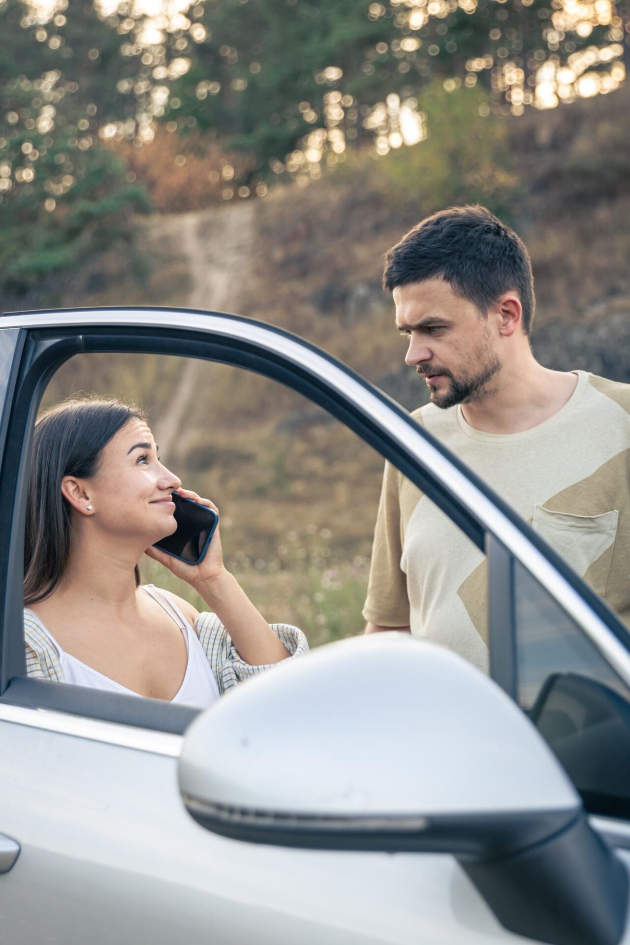 Woman talking on the phone standing near her husband by the car in nature Auto insurance plan